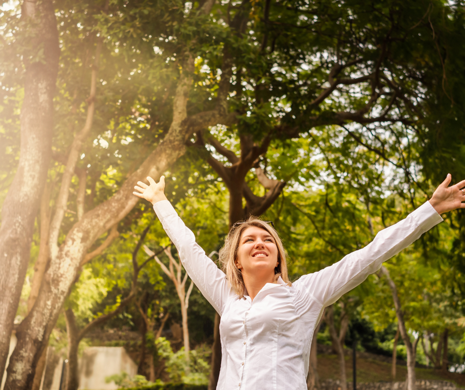 Woman enjoying a walk outdoors, smiling with open arms in soft sunlight